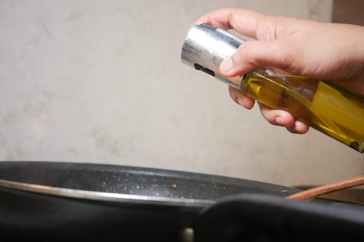 A hand pours olive oil into a skillet, preparing for cooking activity.