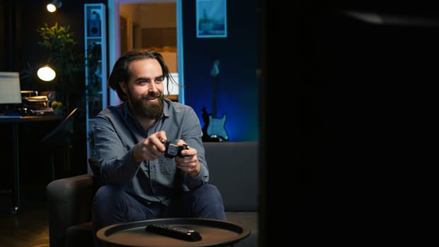 Cheerful gamer rushing home to play newly released game. Happy man jumping on couch, eager to play videogame on console, relaxing after hard day at work, camera B slow motion shot