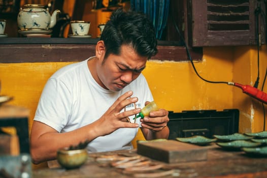 Vietnamese Asian man artisan craftsman works in a jewelry workshop on street in the old town in Hoi An city in Vietnam in Asia. Hoi An, Vietnam - December 2, 2024