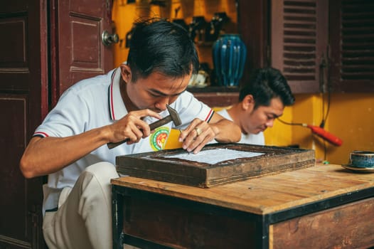 Vietnamese Asian men artisans craftsman works in workshop on street in old town in Hoi An city in Vietnam in Asia. Hoi An, Vietnam - December 2, 2024