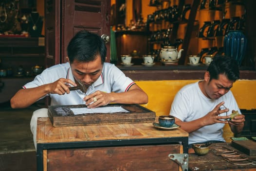 Vietnamese Asian two men artisans craftsman works in workshop on street in old town in Hoi An city in Vietnam. Hoi An, Vietnam - December 1, 2024