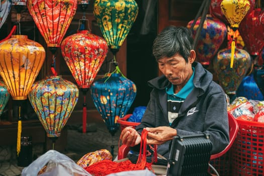 Asian man artisan craftsman makes Vietnamese silk lanterns at ancient town market in Hoi An city in Vietnam. Hoi An, Vietnam - December 1, 2024