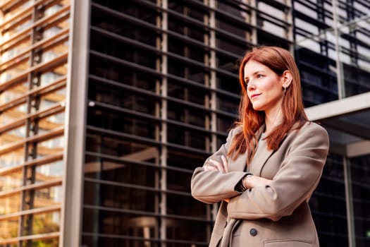 young adult woman in suit jacket standing with arms crossed in front of an office building, concept of entrepreneur and business, copyspace for text