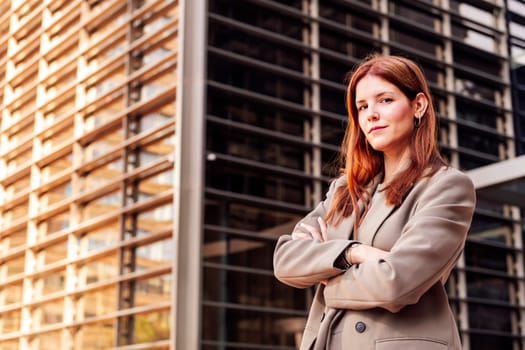 young adult woman in suit jacket standing looking at camera with arms crossed in front of an office building, concept of entrepreneur and business, copyspace for text