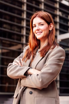 young adult woman in suit jacket standing smiling happy with arms crossed in front of an office building, concept of entrepreneur and business, copyspace for text
