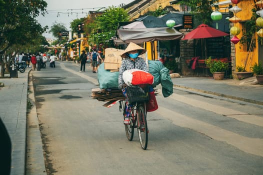 An elderly Vietnamese woman rides a bicycle with trash and cardboard on street in Hoi An City in Vietnam in Asia. Hoi An, Vietnam - December 2, 2024