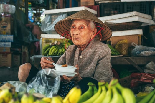 Portrait of an old elderly Vietnamese woman selling fruit at an Asian food market on a street in Hoi An in Vietnam in Asia. Hoi An, Vietnam - December 1, 2024