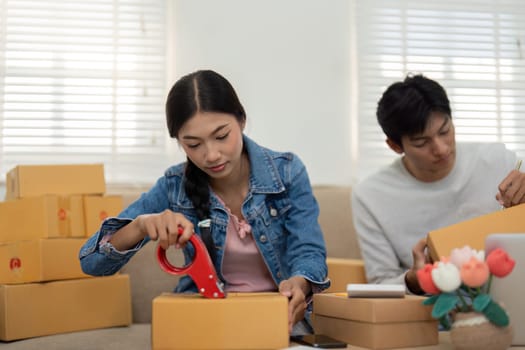 A dedicated entrepreneur uses professional tools to prepare packages, while her teammate focuses on strategic planning to ensure their business thrives.