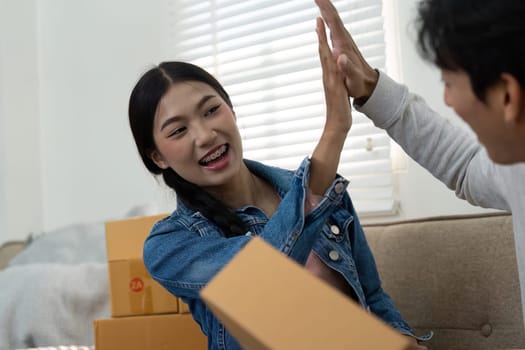 The entrepreneurial duo shares a joyful moment, high-fiving each other after completing a packaging session for their latest product launch, showcasing teamwork and enthusiasm.