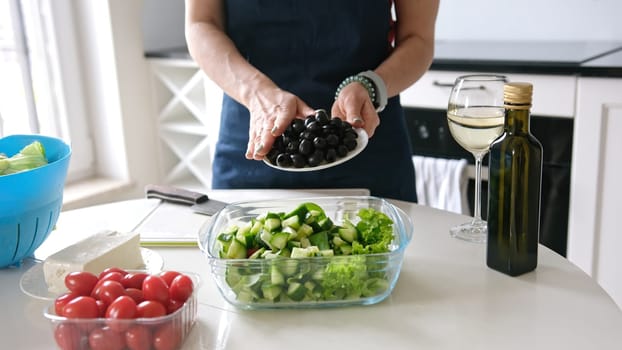Woman At Home Prepares Greek Salad, Pouring Olives Into Salad Bowl