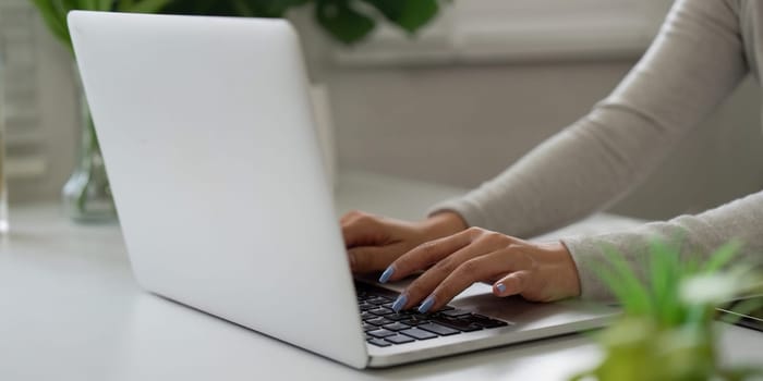 An individual engages in remote work at home, typing on a laptop in a serene setting filled with plants, highlighting the blend of productivity and comfort.