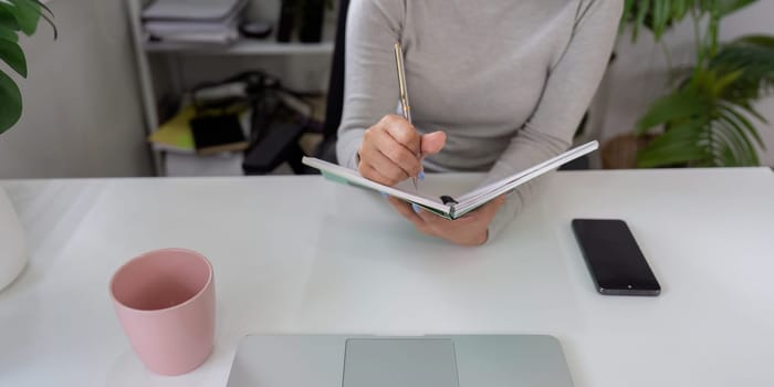 While working from home, a person actively takes notes in a notebook, showcasing a balance of organization and creativity in a tranquil environment.