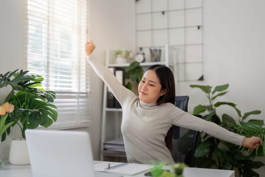 A young woman stretches and refreshes her mind in the comfort of her home office, surrounded by greenery and natural light.