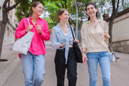 three gossipy teenagers chatting outdoors. A group of Caucasian friends chatting and communicating. Young adult students smiling and walking together at a social gathering.