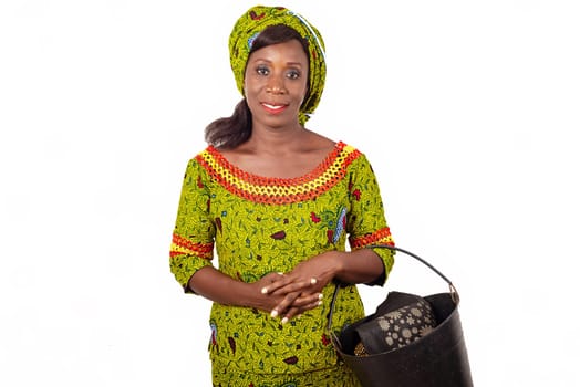 beautiful african adult woman wearing a green loincloth smiled with on the arm a black bucket containing a bag