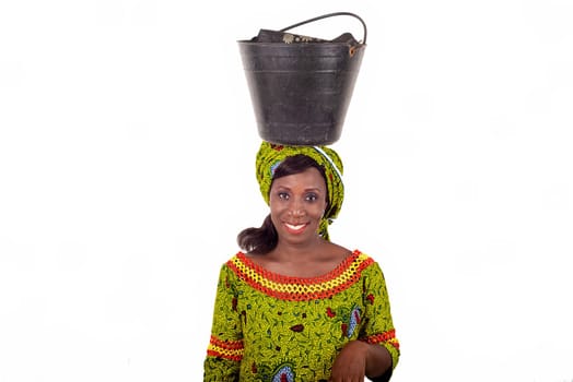 beautiful African adult woman dressed in green loincloth balances a black bucket on her head and accompanied by a beautiful smile