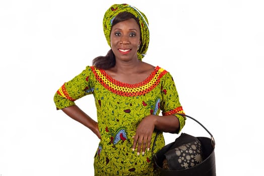 beautiful african adult woman dressed in green loincloth, puts on arm a beautiful black bucket smiling