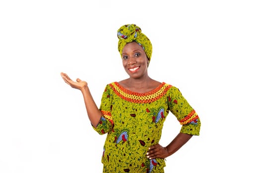 Beautiful african adult woman wearing a loincloth and a green scarf on her head with her arm crossed and her hand raised smiling