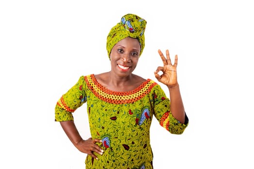 A beautiful optimistic African adult woman wearing a beautiful loincloth and a beautiful green scarf on her head is smiling, showing largely the correct gesture, the excellent mood, while being great