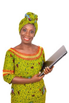beautiful african adult woman dressed in loincloth and green scarf is standing, holding a laptop computer in hand while being smiling