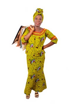 beautiful african adult woman wearing a loincloth and a green scarf is smiling and happy with shopping bags in hand raised and arms crossed