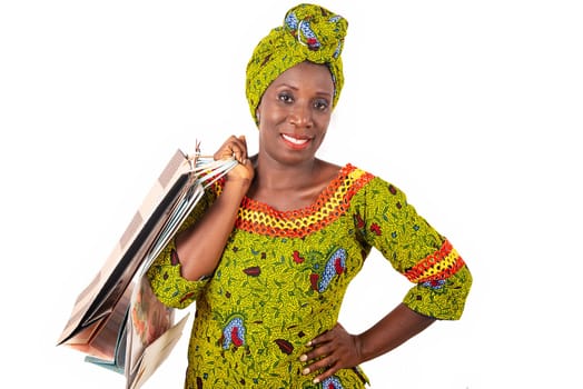 beautiful african adult woman wearing a loincloth and a green scarf is smiling and happy with shopping bags in hand raised and arms crossed