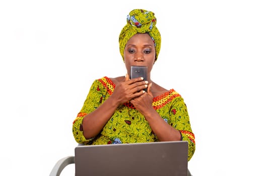 beautiful mature woman sitting in traditional dress on white background communicating with mobile phone with laptop lying on her thighs.