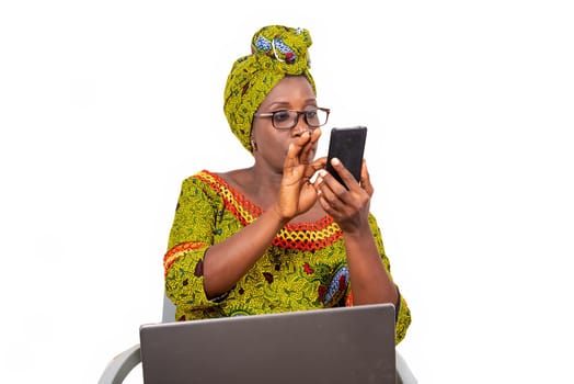 beautiful mature woman in glasses isolated on white background looking at mobile phone with laptop on her thighs.