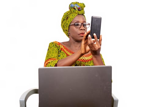 beautiful mature woman in glasses isolated on white background looking at mobile phone with laptop on her thighs.