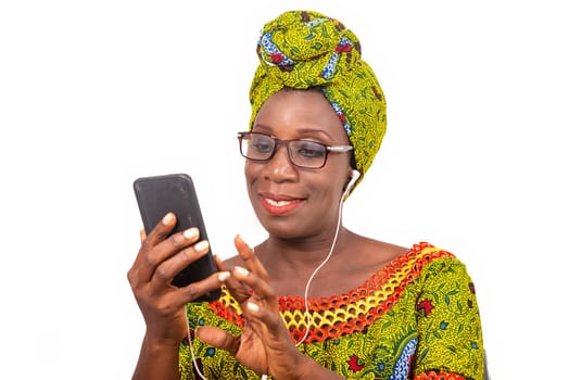 beautiful african adult woman dressed in loincloth and green scarf with glasses, takes pleasure communicating with headphones, in his mobile while smiling