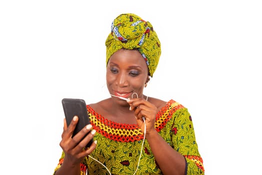 beautiful African adult woman dressed in loincloth and green scarf is communicating with his headphones in his mobile phone while smiling