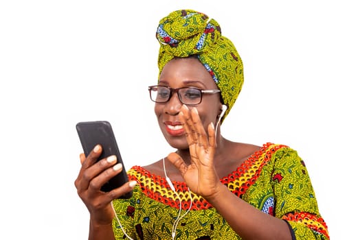 beautiful african adult woman dressed in loincloth and green scarf with glasses, takes pleasure communicating with headphones, in his mobile while smiling