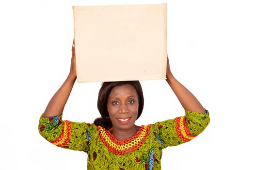beautiful African adult woman wearing a green loincloth with long hair, is standing holding a cardboard box on her head with a beautiful smile