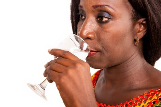 beautiful African adult woman wearing a green loincloth with long black hair, is drinking mineral water in a glass, sideways, on a white background.
health and beauty concept