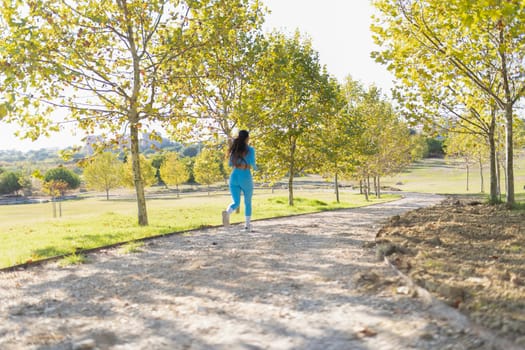 Fit woman jogging in a park with autumnal trees during a sunny day