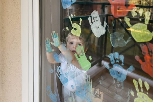 Kid paints with palms on the window. Quarantine Stay at home