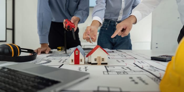 Team members engage in a collaborative planning session, discussing architectural designs and model houses, showcasing teamwork in construction development.
