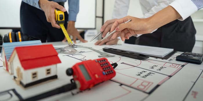Workers are focused on drafting plans, with hands measuring dimensions and placing emphasis on different areas in the architectural layout.