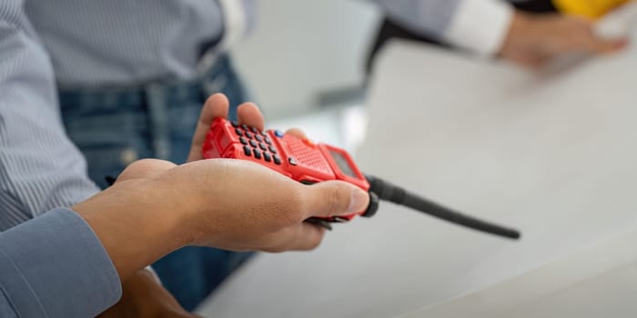 A team member holds a two-way radio, enhancing communication while discussing construction plans during a meeting, showcasing teamwork.