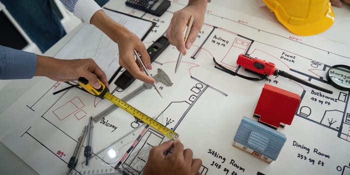 A team of professionals examines architectural plans with tools, measuring spaces actively, and ensuring detailed construction specifications.