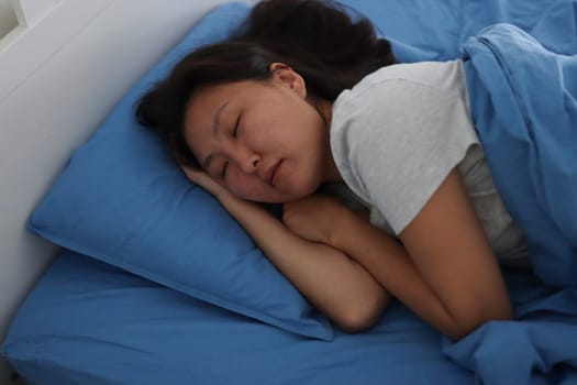 Peaceful sleep enjoyed by young asian woman resting comfortably on blue bedding
