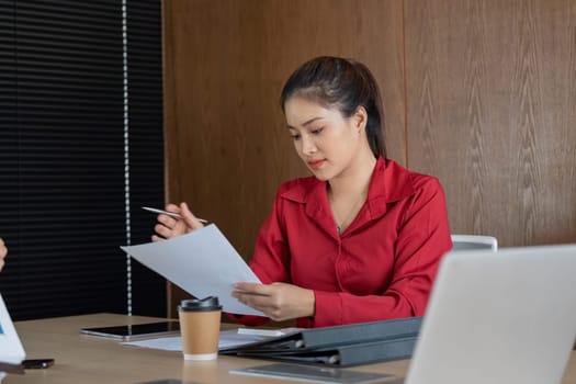 In a collaborative office environment, a woman scrutinizes financial reports while making notes, perfect for conveying professionalism and analytical skills in finance.