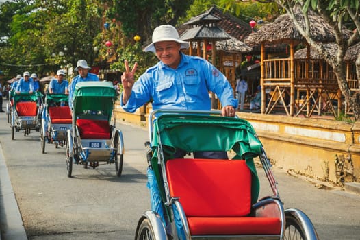 A happy Vietnamese male bicycle rickshaw driver walks down the street in old town in Hoi An in Asia. Hoi An, Vietnam - December 1, 2024