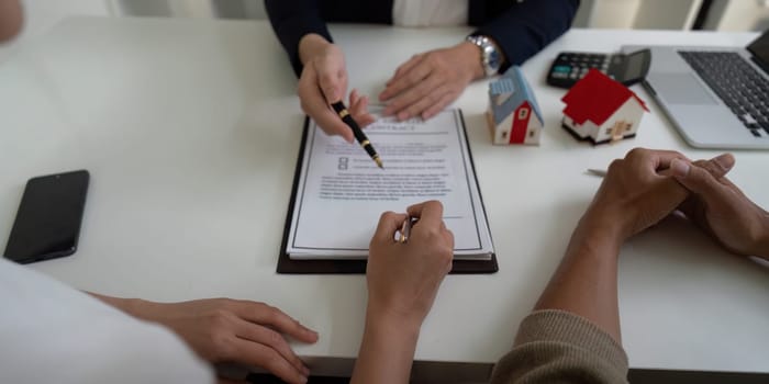 A couple engages with a real estate agent, discussing property details while reviewing and signing contracts in a professional setting focused on home buying.