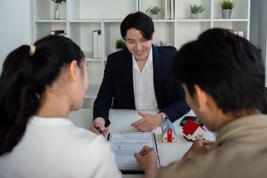In a sleek office environment, a couple consults with their real estate agent about potential property purchases, examining contracts and models during the process.