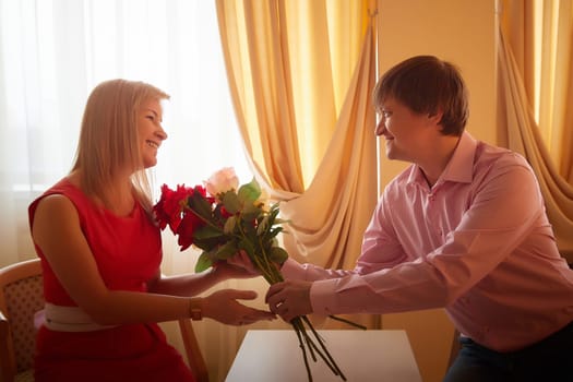 A couple exchanges flowers during a romantic photo shoot in a hotel room, celebrating their love for Valentine's Day.