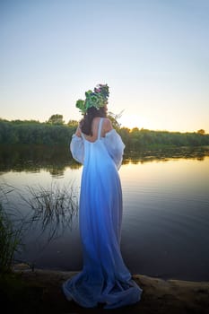 Slavic plump chubby girl in long white dress on the feast of Ivan Kupala with flowers and water in a river or lake on summer evening