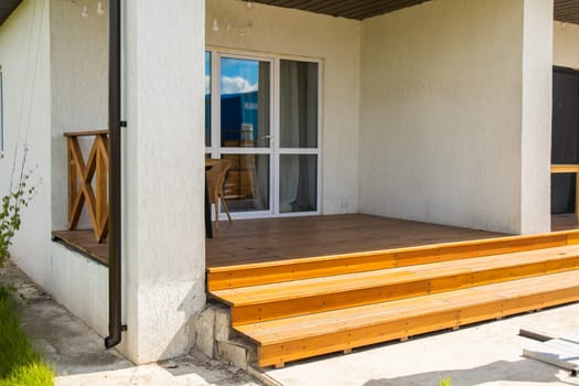 Wooden terrace with glass door and wicker chair. Functional residential architecture and smooth transition between home and outdoor space.