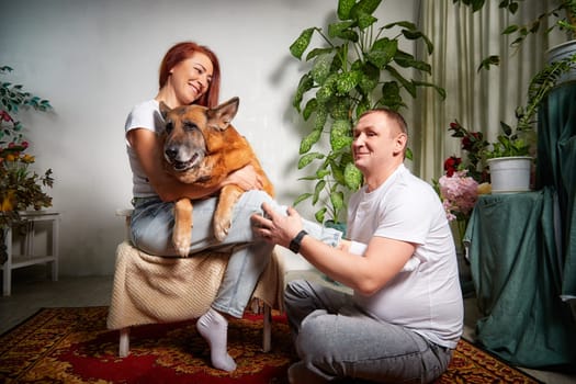 A couple spends quality time together as they play with their happy German Shepherd indoors, surrounded by greenery.