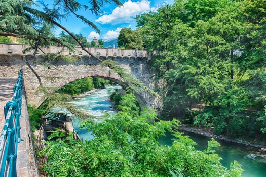 View of Steinerner Steg bridge crossing a river with lush green trees on both sides, iconic landmark in Merano, South Tyrol, Italy